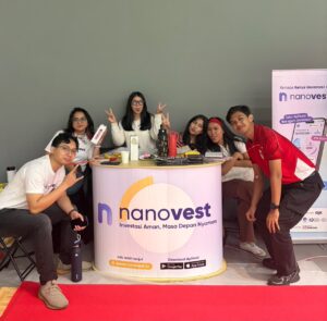 Group of six young people posing at a Nanovest promotional booth with a curved counter and banner on the right.